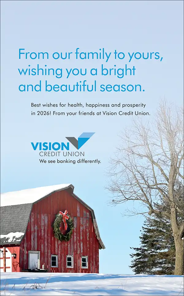 A red barn with a holiday wreath sits in the snow beneath a clear blue sky. Bare trees stand nearby. Text above shares a seasonal greeting from Vision Credit Union, wishing health and happiness for 2026.