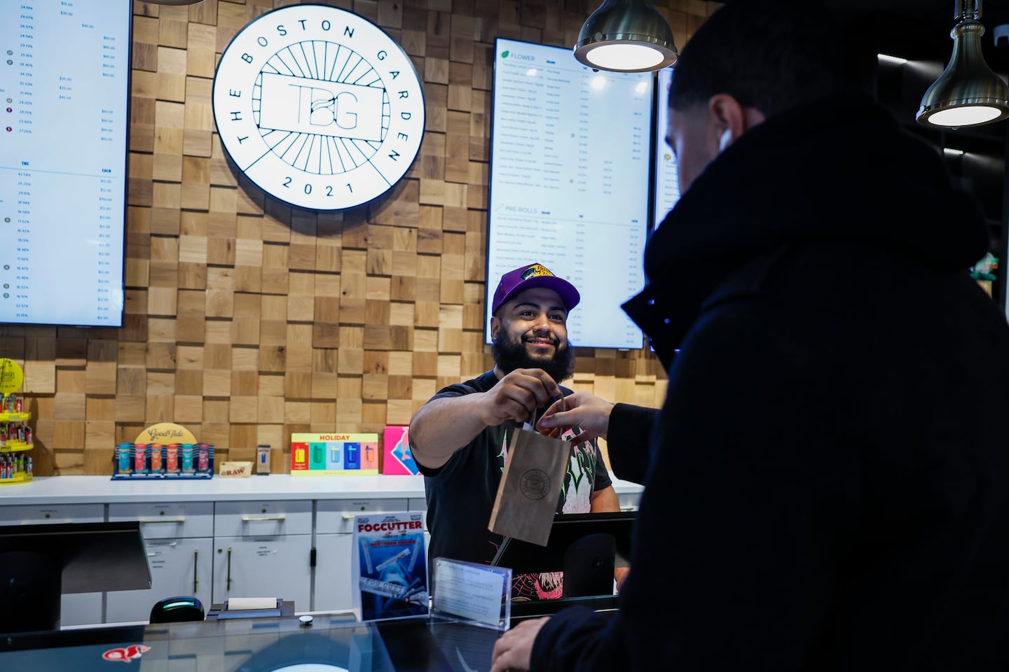 Tony Muñoz, a cannabis expert at The Boston Garden Dispensary, hands a purchase to a customer inside the Cambridge store on Feb. 26.