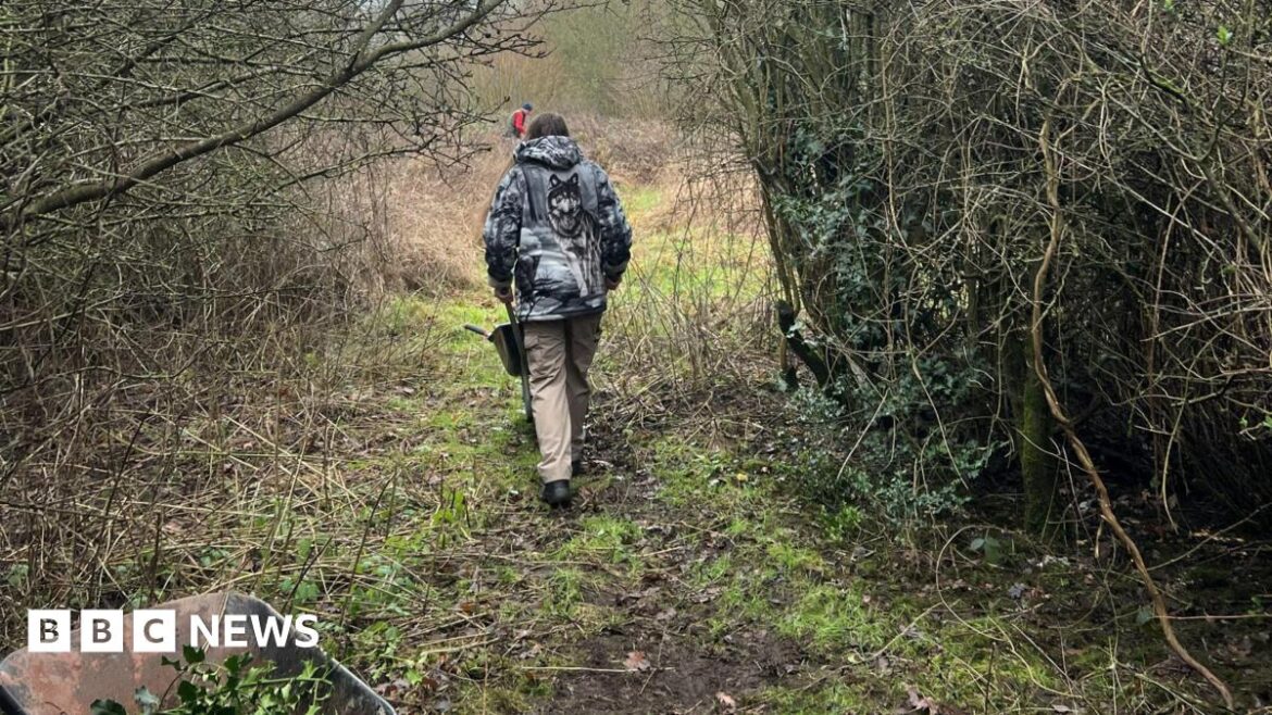 A man with grey hair, wearing a black suit jacket, blue tie and light blue shirt, stands and smiles outside a town hall.