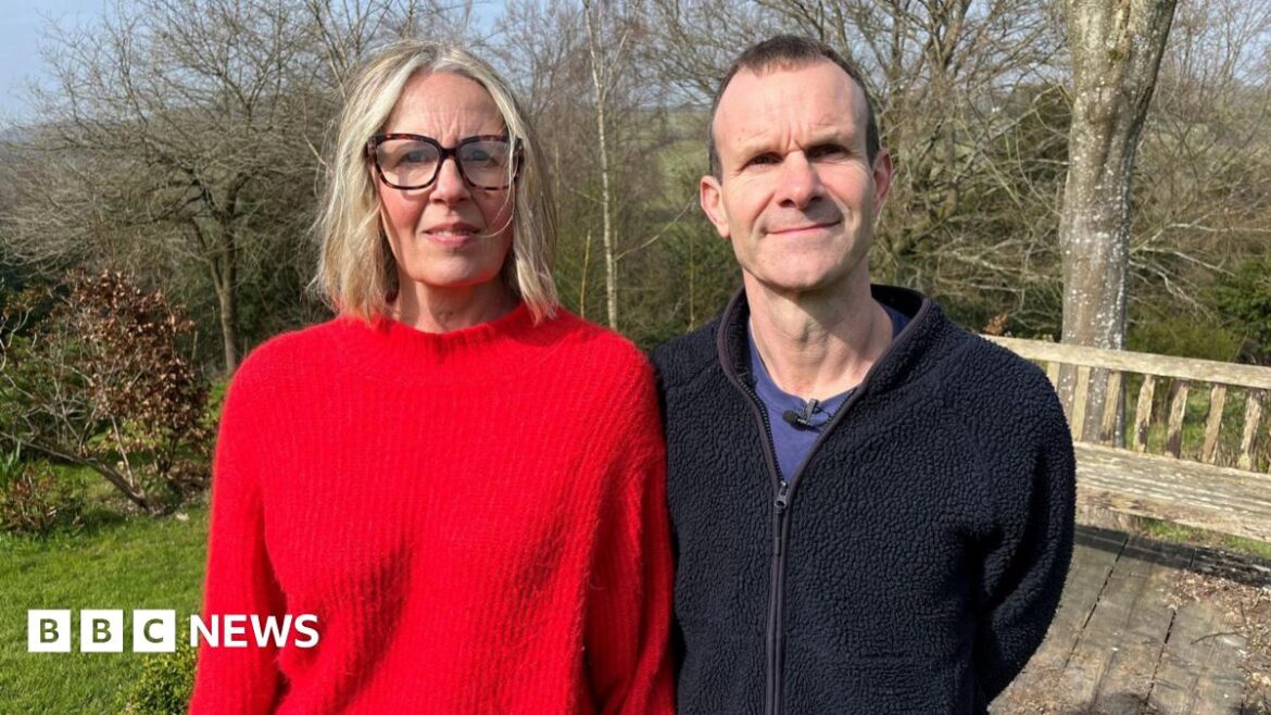 Mystery over raw sewage leak into couple’s Lamberhurst garden Tracey and James Parfitt pictured at her home in Lamberhurst, Kent. Tracey is wearing a red jumper and is looking at the camera. She is wearing a red jumper and has blonde hair. James is wearing a blue t-shirt and black fleece. He has brown hair.