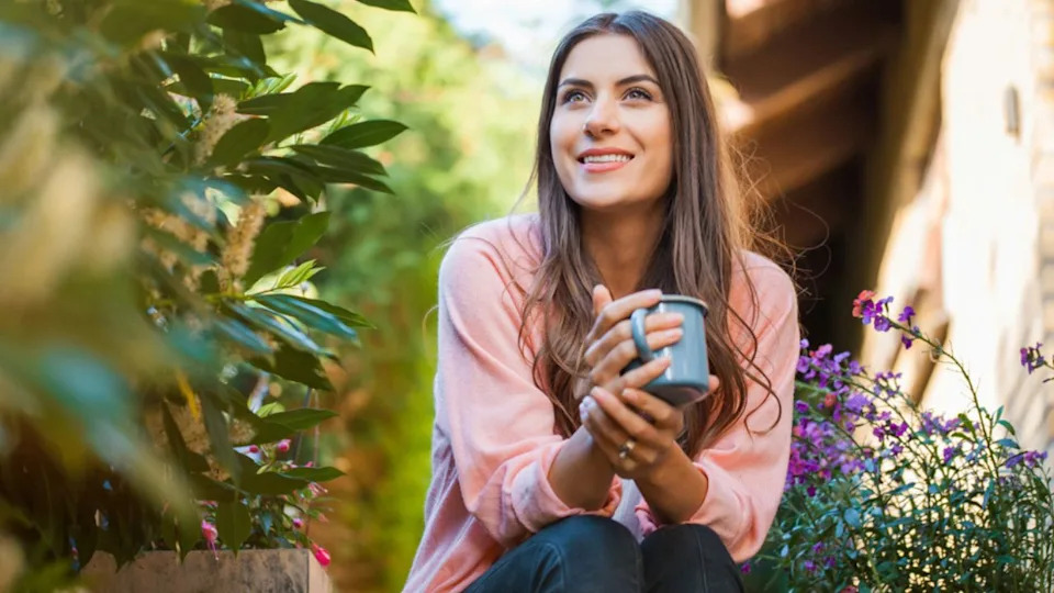 woman enjoying coffee in her garden with purple flowers
