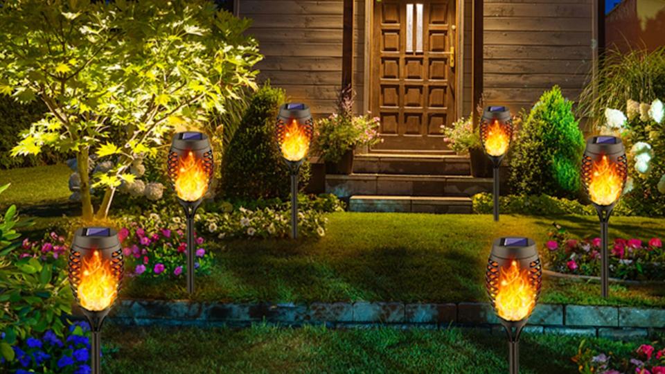 Six solar-powered torch lights on a lawn leading up to the front door of a house.