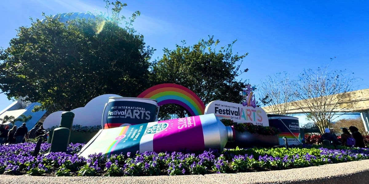 Paint tubes, a rainbow, and festival signs pop among purple blooms as Disney dazzles EPCOT guests—enchanting crowds until 2027 ends.