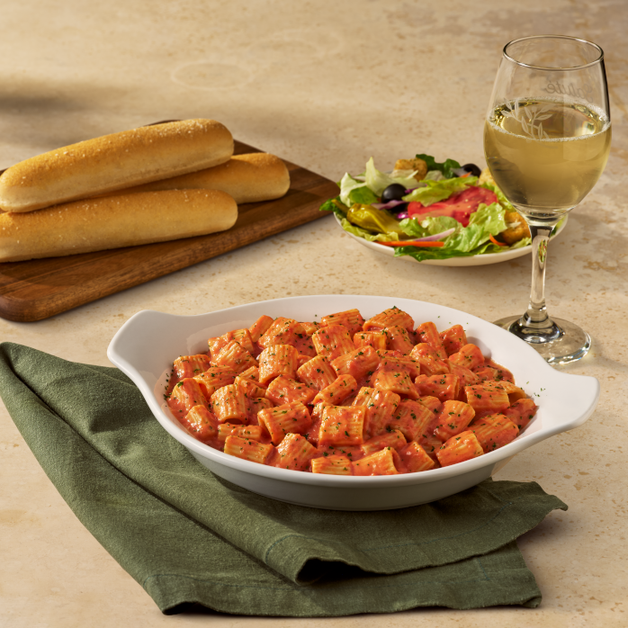 a meal setup with pasta breadsticks salad and wine