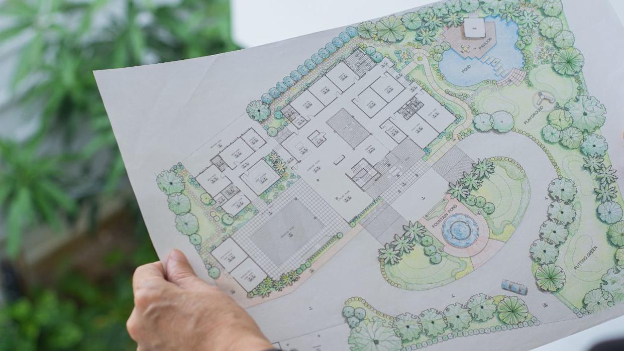 paper sheet of layout plan with hands and garden background, that shown design of house landscape or garden design drawing by hand with color marker pens and color pencil, selective focus