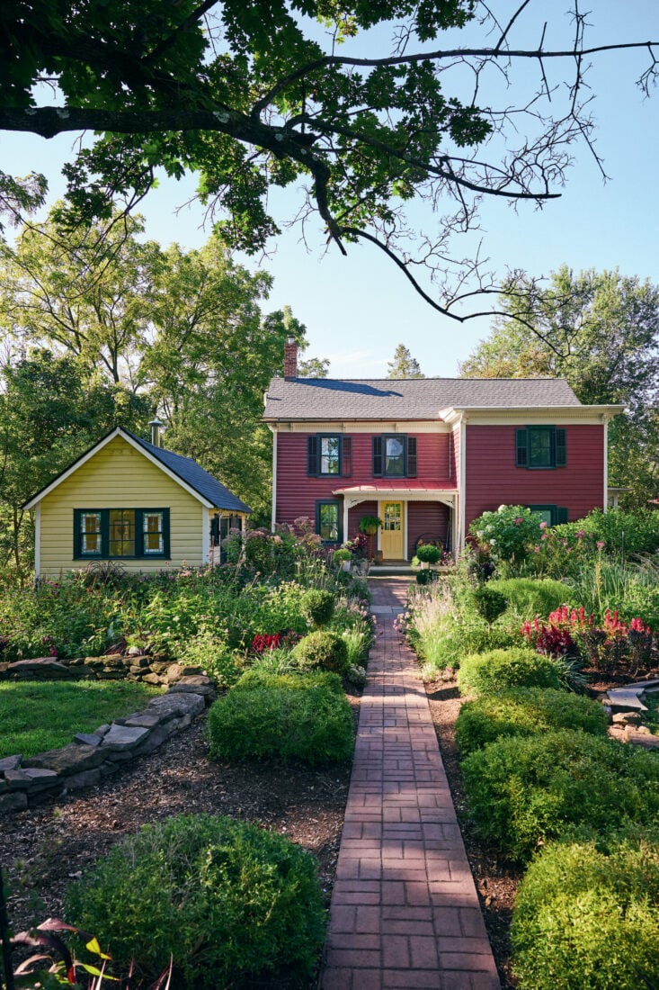 A red house with a lush garden and yellow shed