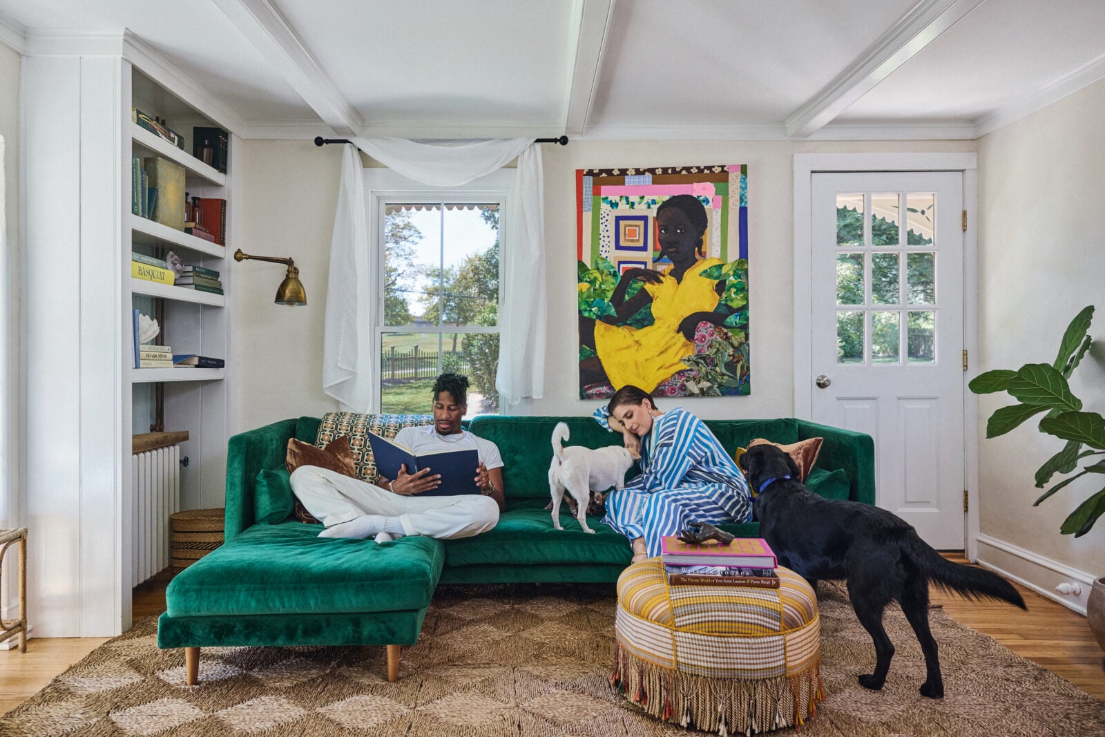 A man and woman on a green couch with two dogs in a living room with colorful decor