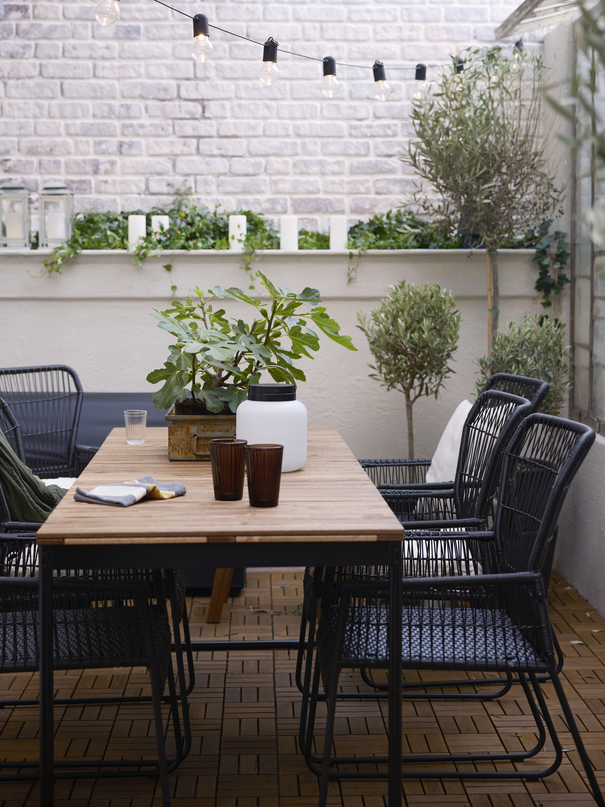 IKEA extendable table on an outdoor balcony with greenery, black dining chairs, string lights, and potted plants