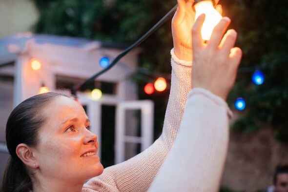 Woman installing colorful party light in back yard.