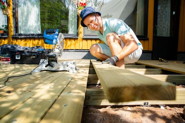 Man building wooden deck in backyard. Authentic DIY home improvement project during summer. Outdoor house renovation and construction.