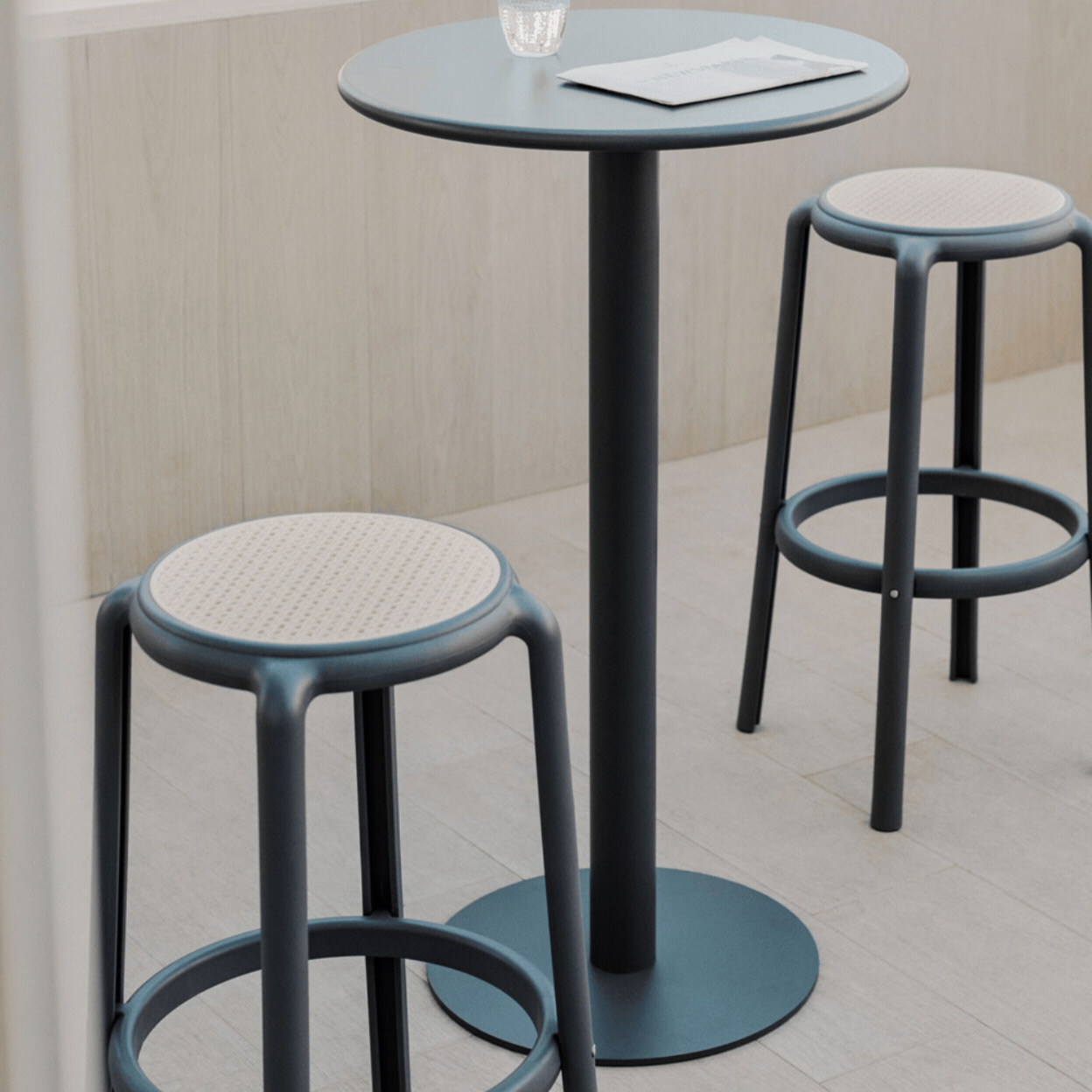 Round High Table Set &Oslash;60 Cm in Mizzi Iron and 2 High Garden Stools in Omara Polypropylene in a rotating gif showcasing it in a naturally lit terrace and as a product against pale green background.