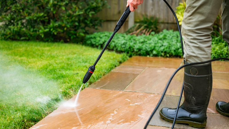 Person wearing rubber boots pressure washing their back patio
