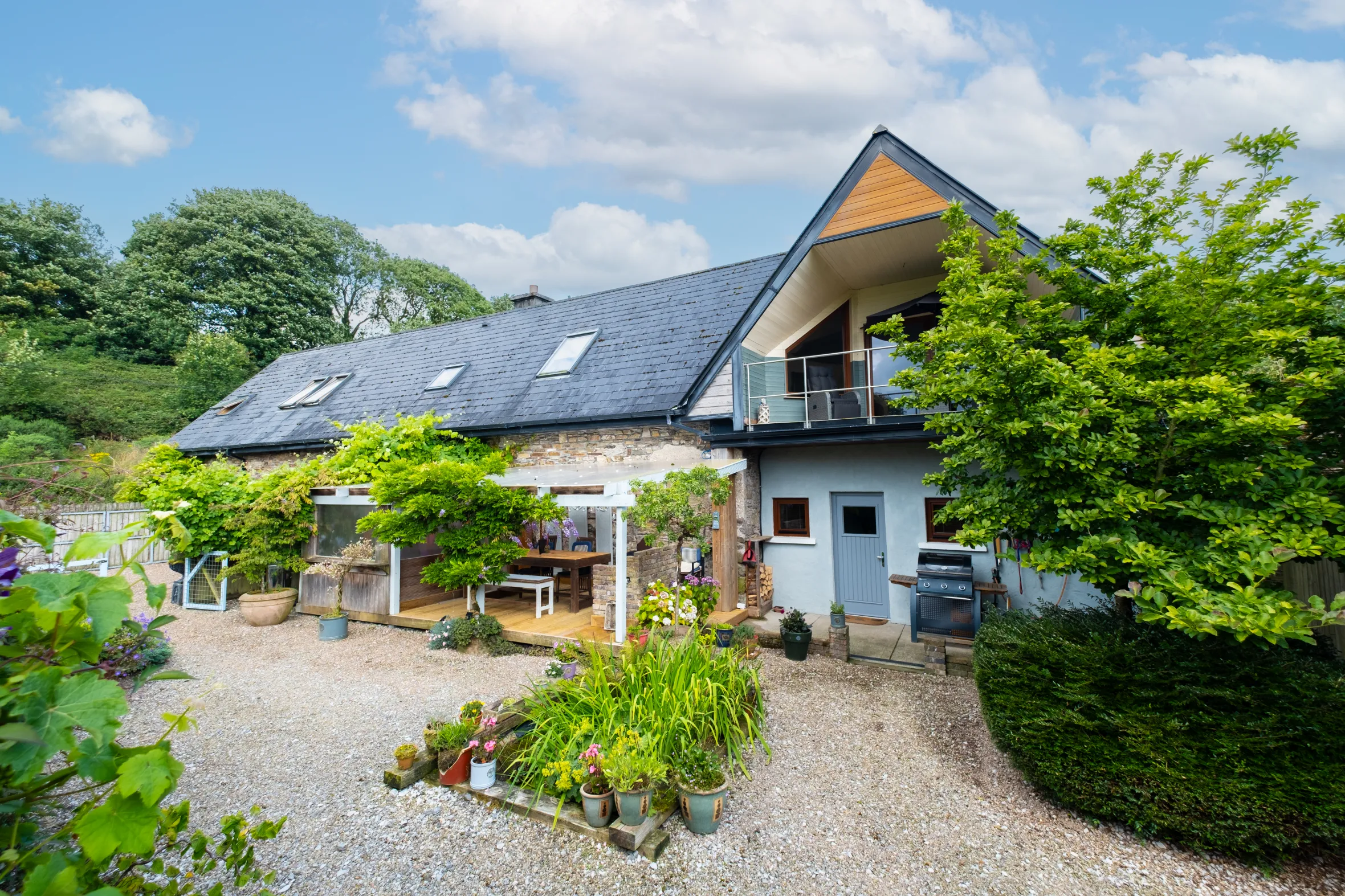 Exterior view of a house with a gravel driveway, an outdoor seating area, and lush green landscaping.