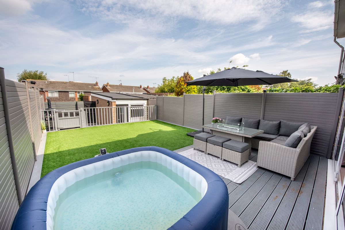 A general view of a small back garden with grey rattan sofa and table, inflatable hot tub artificial grass lawn and composite patio decking and fence.