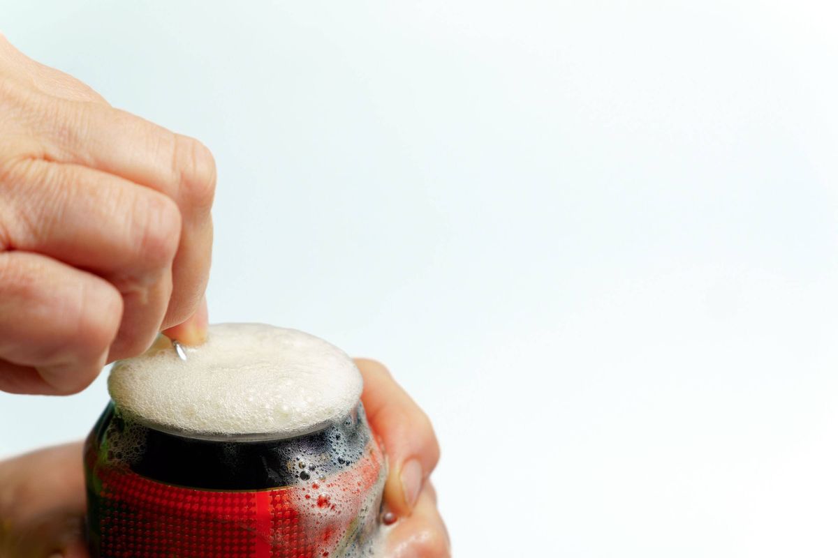 Hand opening beer can with overflowing foam