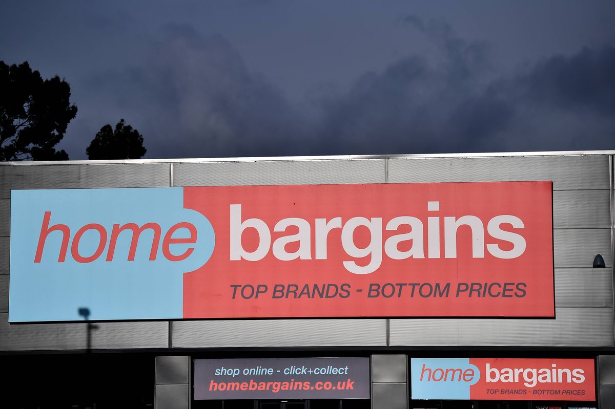 An illuminated signboard prominently displays the words "home bargains" with a tagline in smaller font beneath it, set against a backdrop of a cloudy sky and distant trees.