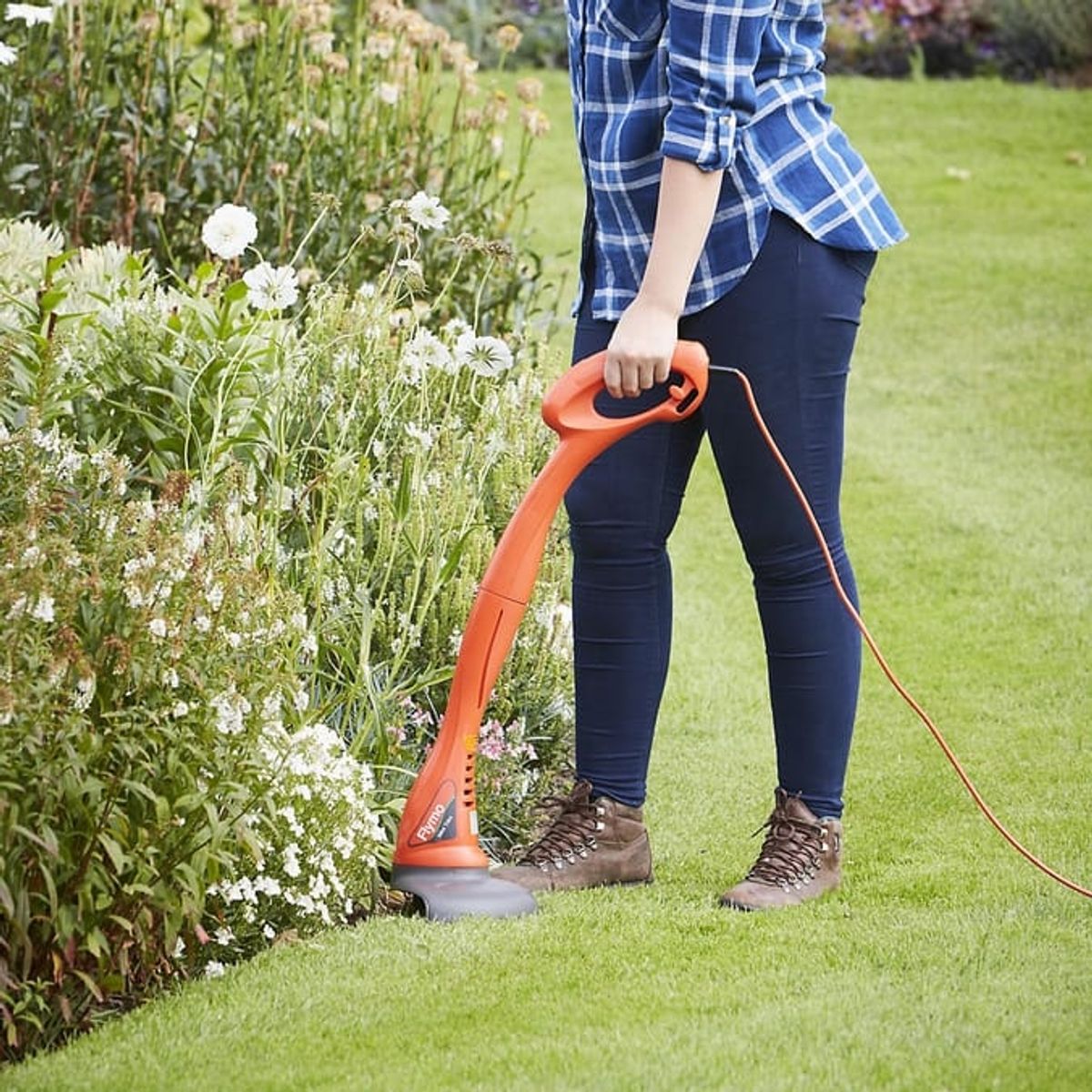 Someone using the orange grass trimmer from Home Bargains to trim the edges of a lawn by a flower bed.