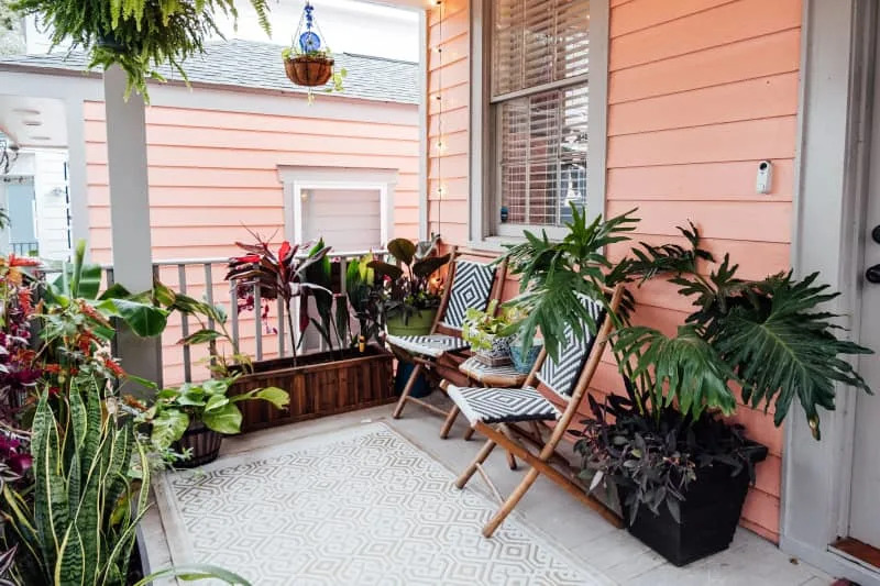 Small porch with pink siding, patterned chairs, and various potted plants.