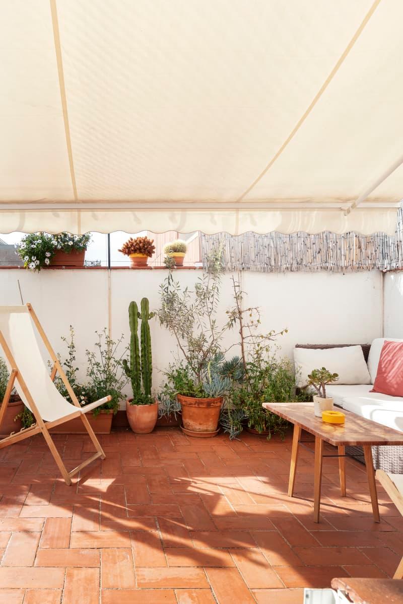 Terracotta patio with potted plants, a deck chair, and a wooden table under a canopy.