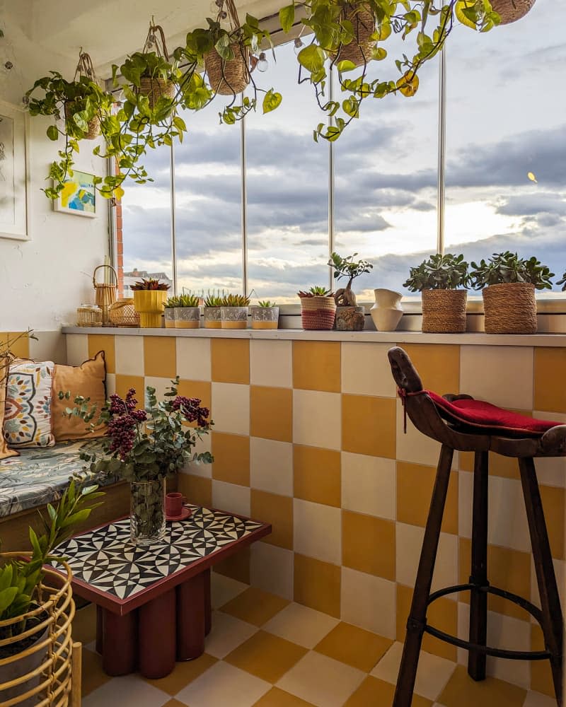 white sunroom with yellow and white checkered wall detail, fabric nestled bench, hanging and potted plants
