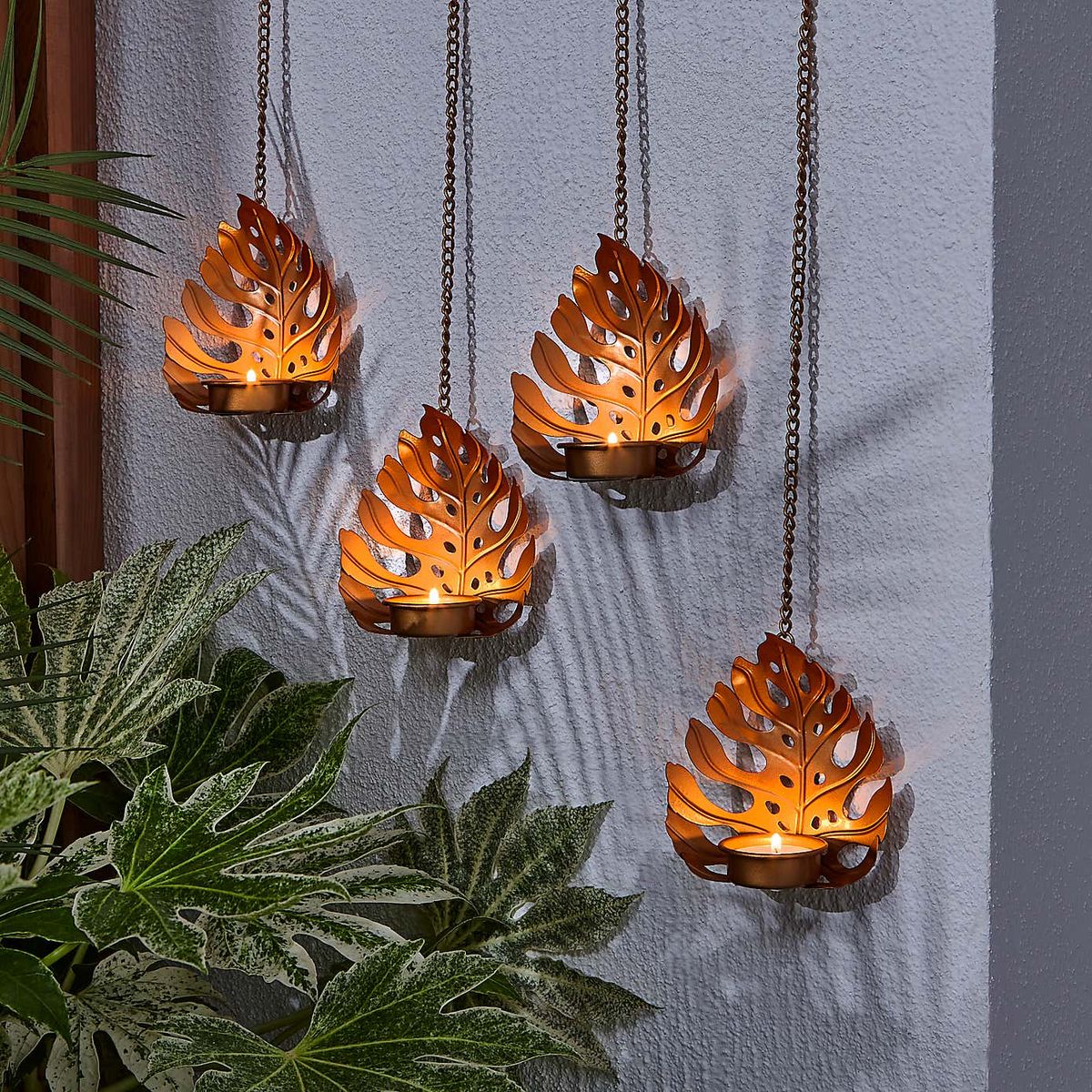 An image of leaf-shaped hanging tealights on a garden wall