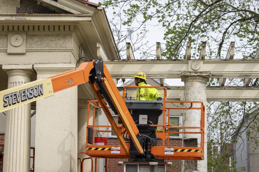 A worker on a lift inspects the trellis and west portico of the pergola at Sears Sunken Garden.