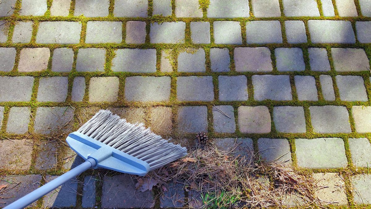 Spring garden cleaning with a broom on stone pavement.