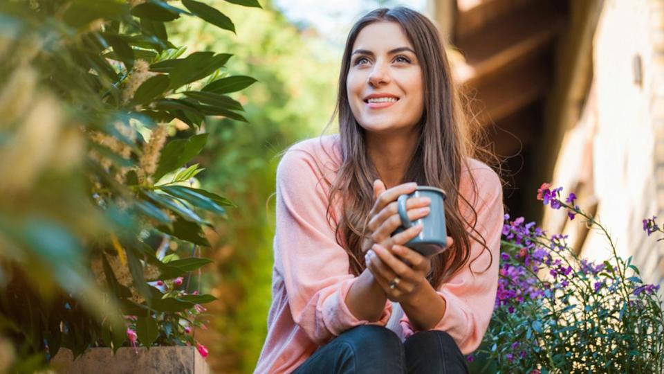 woman enjoying coffee in her garden with purple flowers