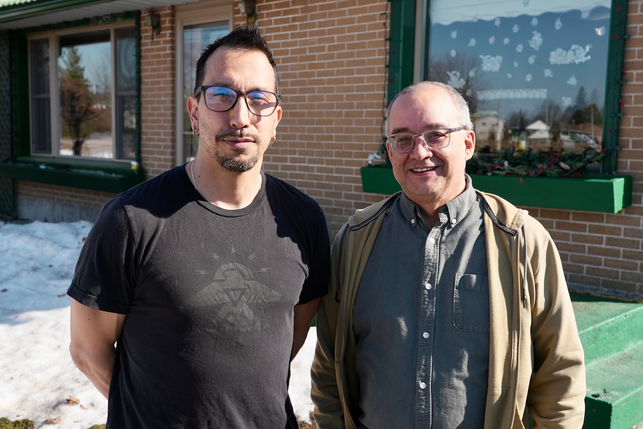 Two men smile and pose next to one another outside.