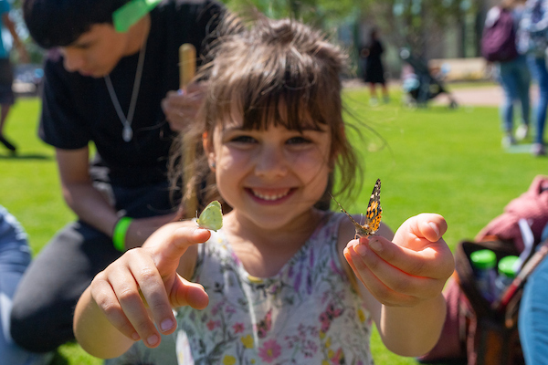 A young girl holding two butterflies, one on each had. 