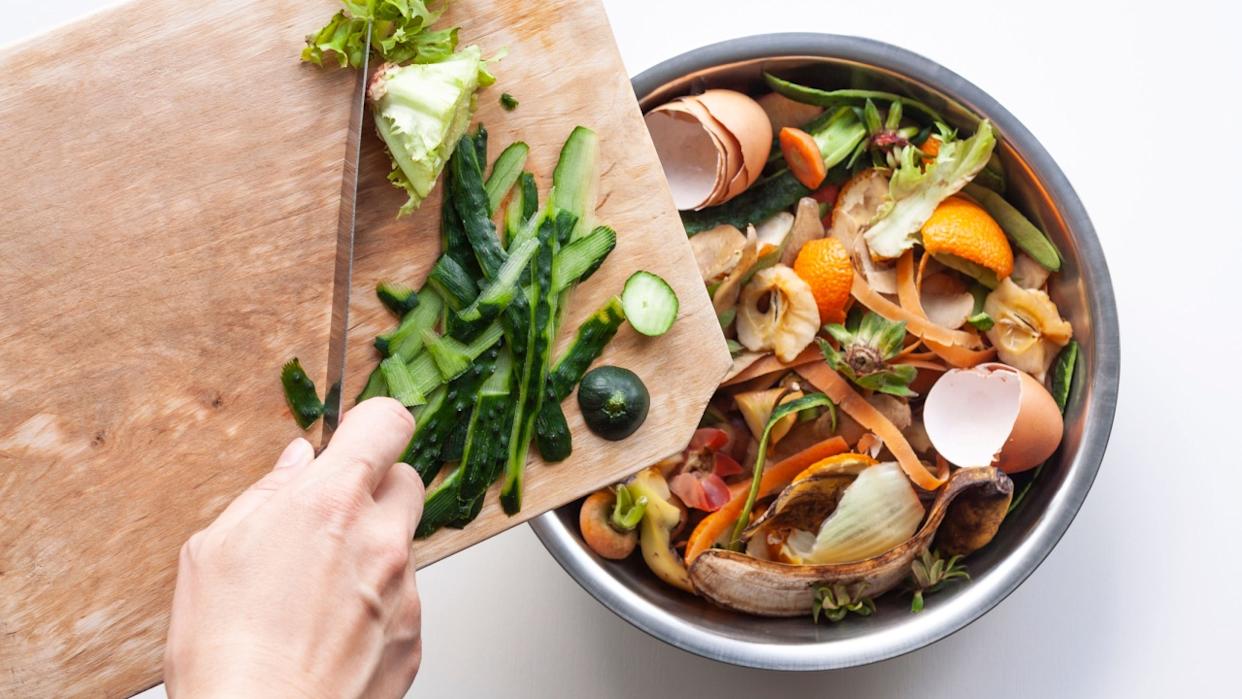 Vegetable peels are thrown from cutting board into an iron bowl with organic food waste. Food leftovers ready to compost. Environmentally responsible behavior, ecological, recycling waste concept.