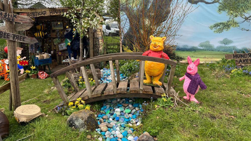 Winnie the Pooh and Piglet characters stand on a bridge over a stream made out of pebbles.