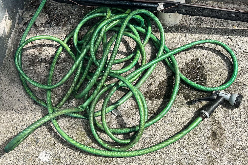 Garden hose coiled on concrete near a wall and door.