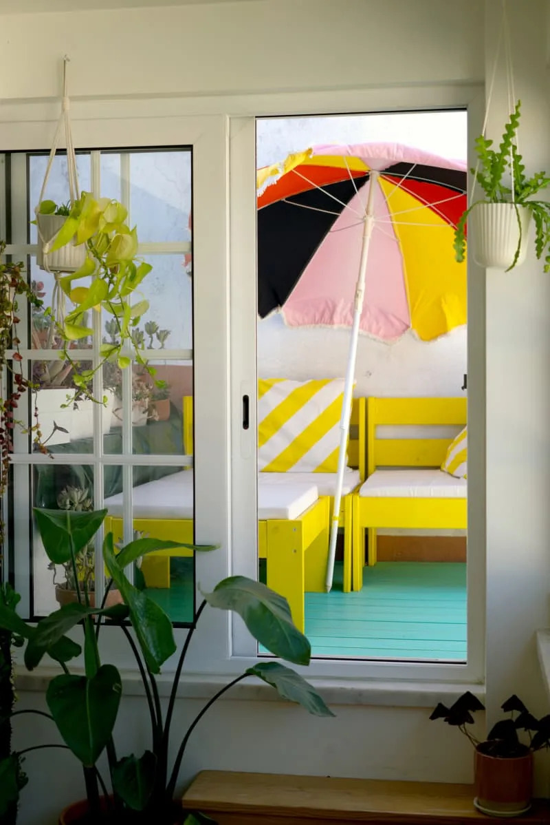 View out to teal deck with yellow chairs and colorful umbrella