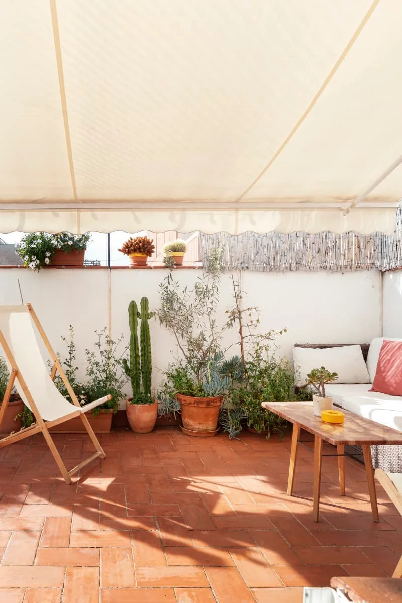 Terracotta patio with potted plants, a deck chair, and a wooden table under a canopy.