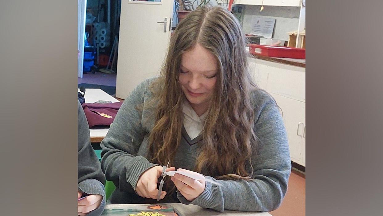 A teenage girl sat at a table cutting pieces of paper.