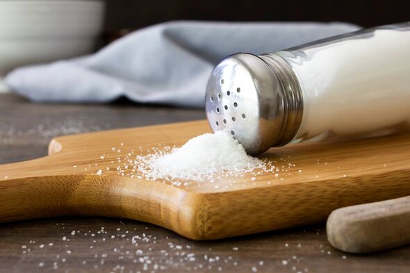 A close up shot of salt spilling out of a salt shaker on to a wooden chopping board. Shot on a rustic wooden kitchen table with A close up shot of salt spilling out of a salt shaker on to a wooden chopping board. Shot on a rustic wooden kitchen table with