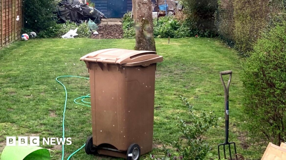 A brown wheelie bin, placed on the grass in the garden.