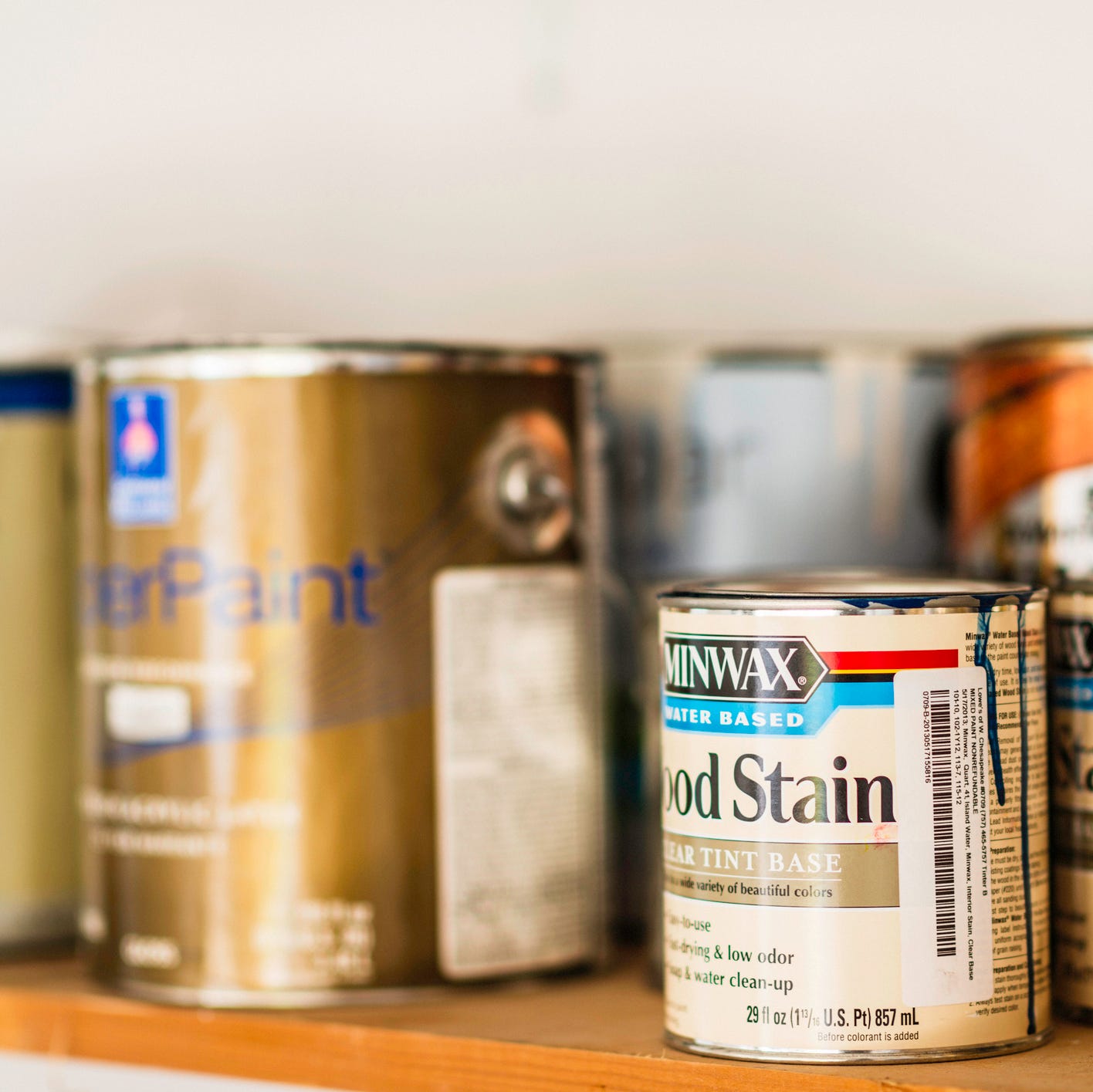 assorted cans of paint, spray paint and wood stain on a wood shelf