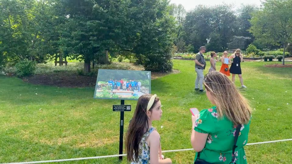 Visitors look at a sign in near the White House Kitchen Garden, featuring First Lady Melania Trump participating in a harvesting and planting event with the Boys and Girls Club of Greater Washington September, 2017 during the White House 2026 Spring Garden Tour on Saturday. - Riane Lumer/CNN