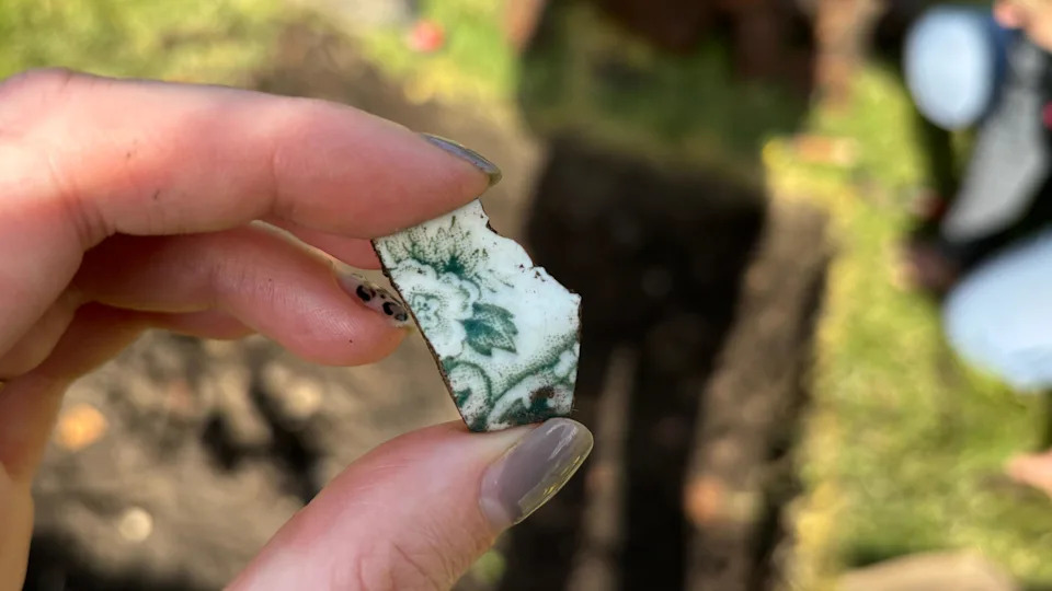 A view of someone holding a tiny shard of white pottery with a flower design.