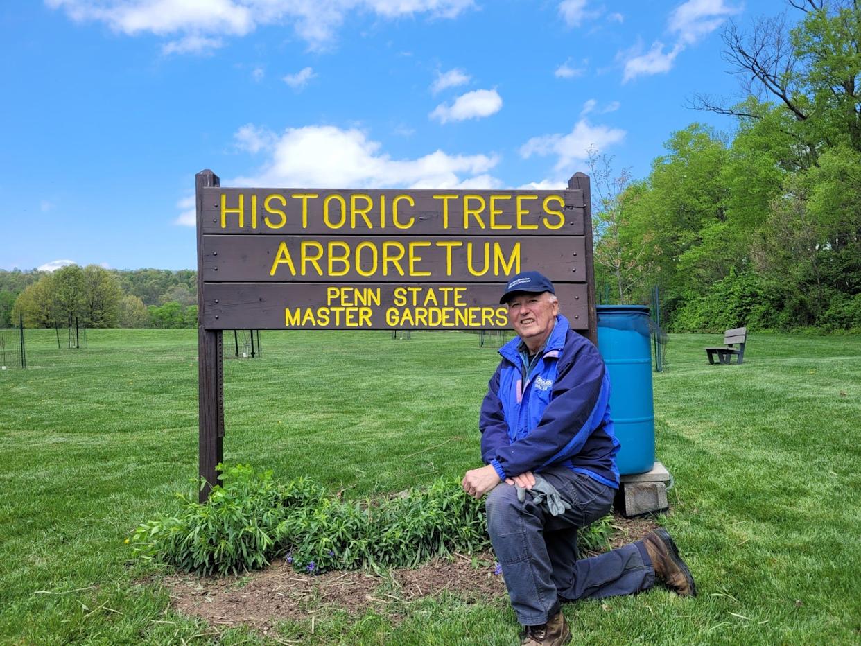 Master Gardener and Historic Tree Arboretum Chair Dean Emig kneels in front of the sign at the Historic Tree Arboretum at John Rudy Park in York.