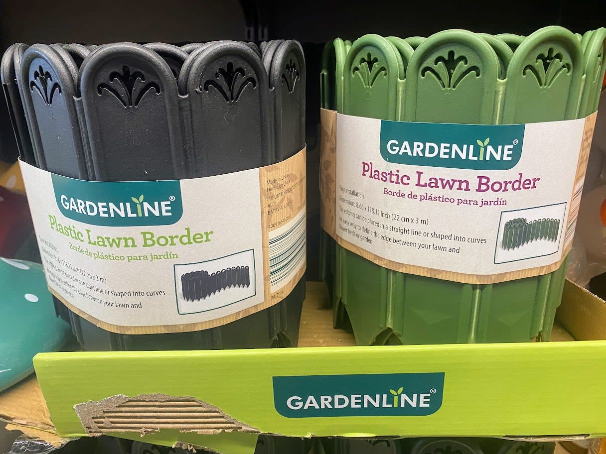 Two rolls of Gardenline Plastic Lawn Border, one black and one green, are displayed on a store shelf in a yellow cardboard box labeled "Gardenline.
