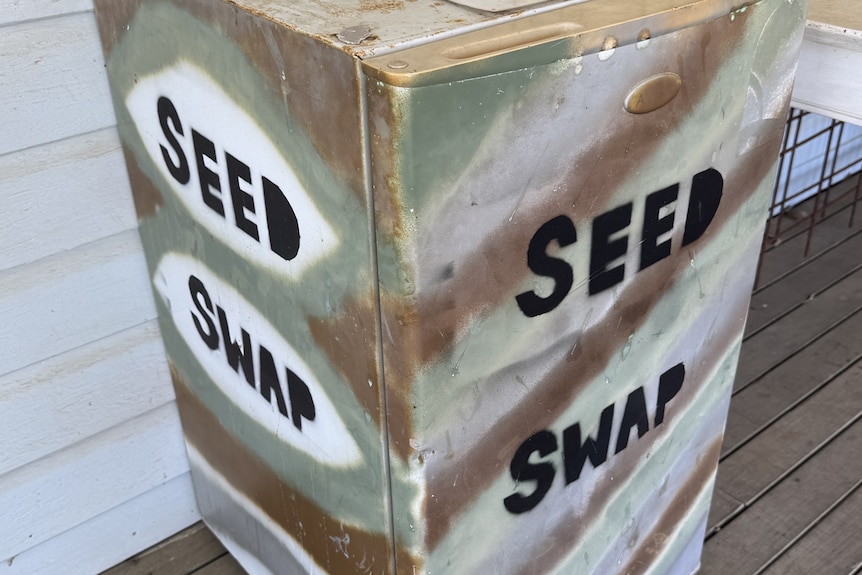 A bar fridge with the words "SEED SWAP" painted on it sits on a verandah.