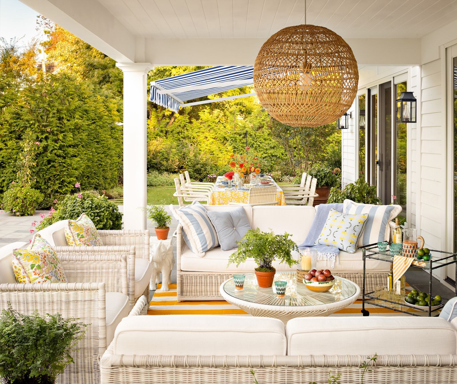 Covered patio with couches wicker pendant light and a bar cart.