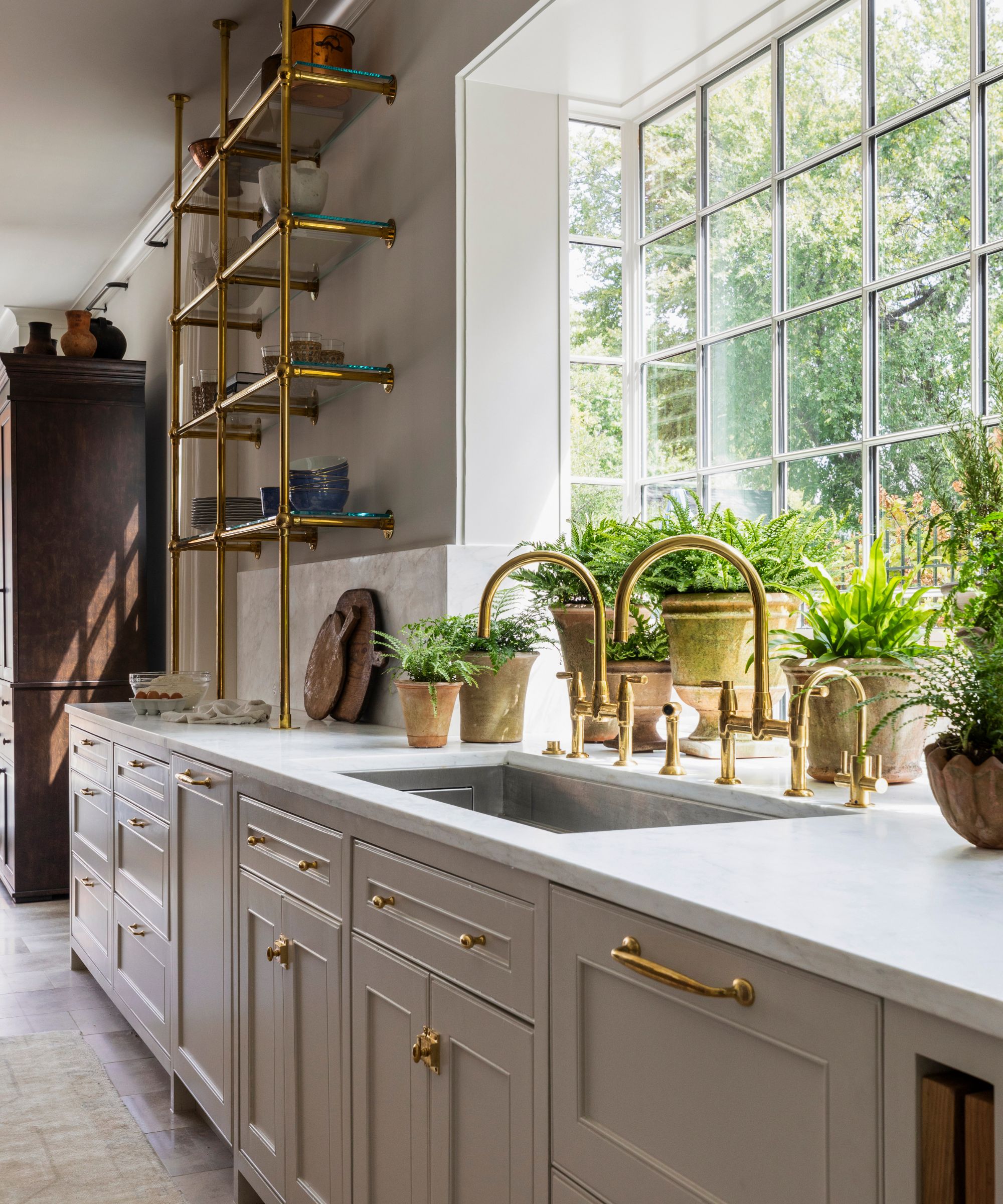 A neutral kitchen with a large window filled with potted herbs