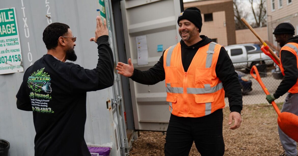 Mario Monteiro Was Incarcerated at 17. Prison Gardening Grew Him Up. A photo of a man in an orange safety vest greeting another man in a black shirt. Both men have a medium skin tone and beards.