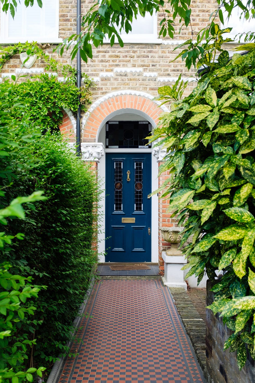 Elegant blue door of traditional london victorian house with checkered pathway and green bushes victorian architecture featuring a blue door, checkered pathway, and lush green bushes, evoking classic london style