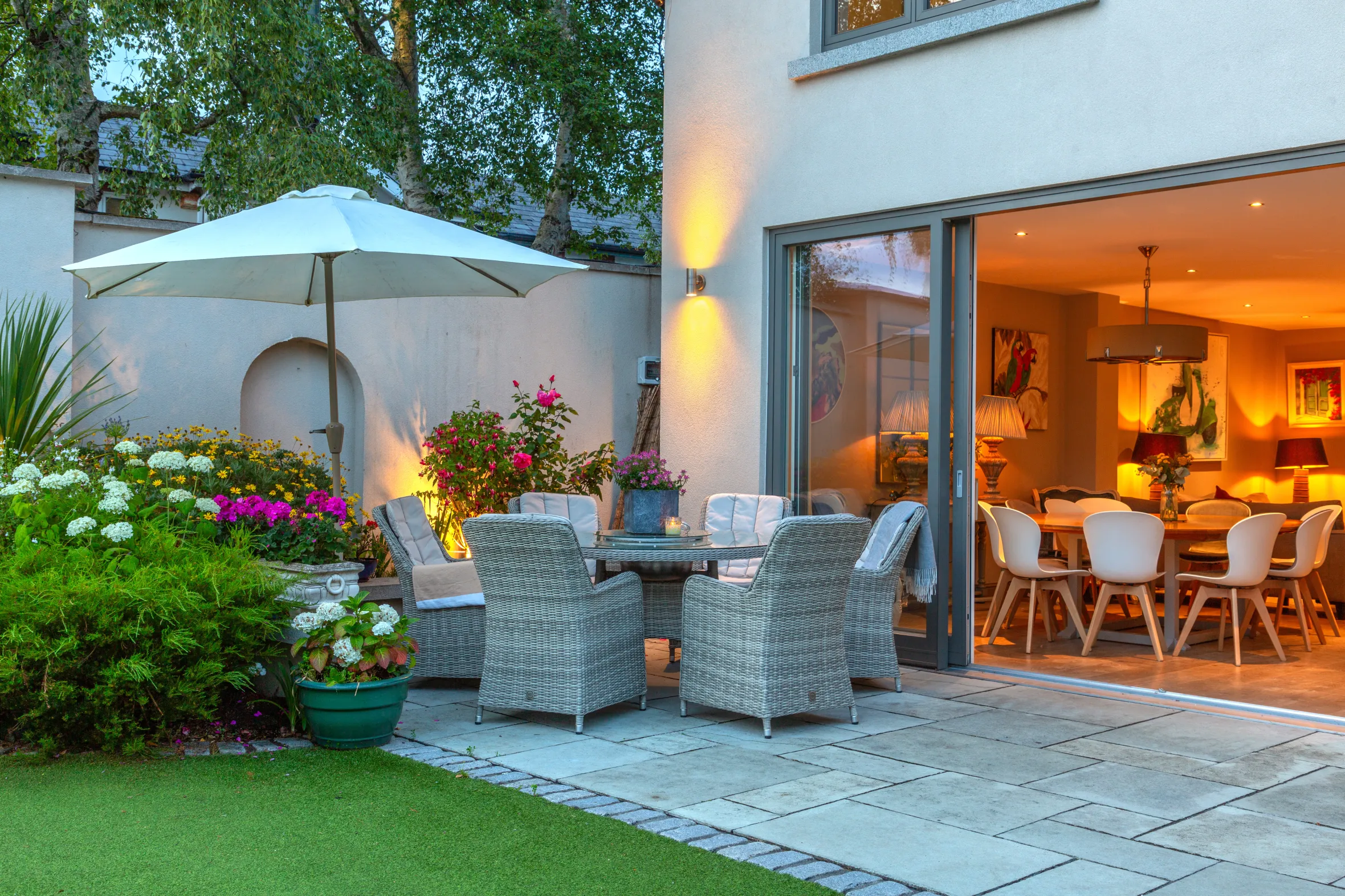 An outdoor patio with wicker chairs and table and an open sliding glass door leading to a dining room.
