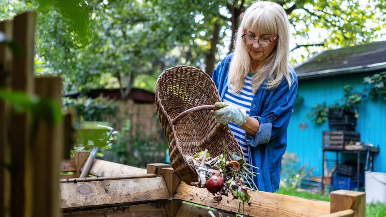 Senior woman throwing vegetable scraps into a compost heap in the backyard
